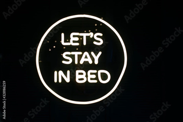 Fototapeta Phrase Let's stay in bed written in shiny neon letters on black background