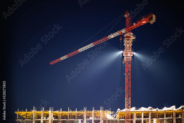 Fototapeta Construction crane in night illumination, construction of a multi-storey modern residential building. Night construction site, twilight spotlight