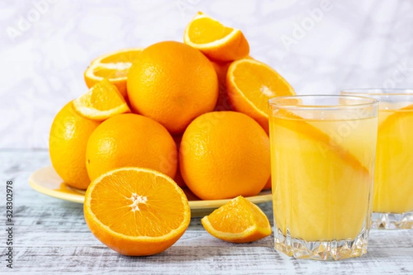 Fototapeta Glass of orange juice and a plate with oranges on a wooden table. Freshly squeezed orange juice.