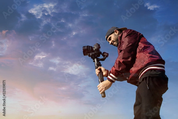 Fototapeta Caucasian videographer filming with cinema gimbal video dslr at sunset , professional video, video maker in event. Cinema lens on gimbal. Medium shot low angle