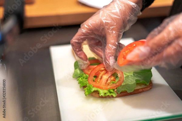 Fototapeta The girl makes a vegetarian sandwich, puts a tomato on the bread.