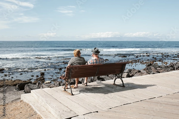 Obraz Elderly couple of tourists at a sea resort on a sunny summer day. Tourism and travel, vacation. Tropical island Tenerife landscape.