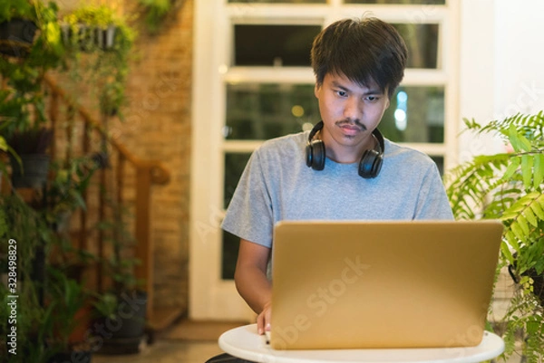 Fototapeta Young man using laptop listening to music on headphone