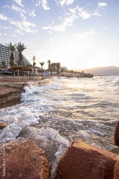 Fototapeta sunrise on the beach. beautiful summer scenery. rocks on the sand. calm waves on the water. clouds on the sky. wide panoramic view