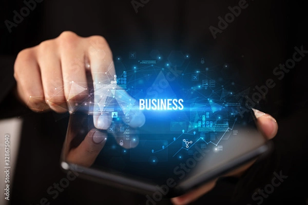 Fototapeta Businessman holding a foldable smartphone with BUSINESS inscription, business concept