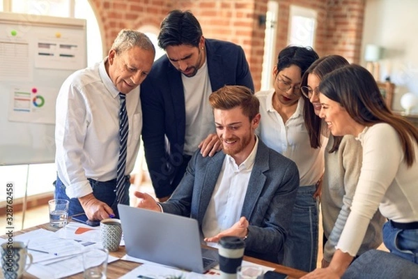 Fototapeta Group of business workers smiling happy and confident. One of them sitting and partners standing around. Working together with smile on face looking at the laptop at the office