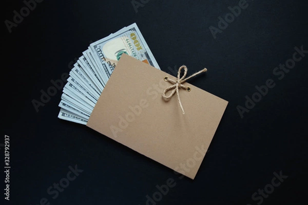 Fototapeta US hundred dollar bills in a Kraft paper envelope and tied with string on a bow on a dark background