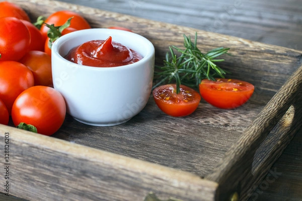 Fototapeta ketchup in a bowl , halves of fresh tomatoes , sprigs of rosemary and whole tomatoes close-up. background with ketchup, tomatoes, rosemary.