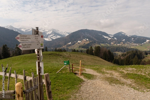 Fototapeta Signpost on the Hündle, a summit in the Allgäu, with a magnificent view over snow-covered mountains and green valleys and a hiking trail