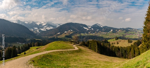 Fototapeta Panorama on the Hündle, a summit in the Allgäu, with a magnificent view over snow-covered mountains and green valleys and a hiking trail