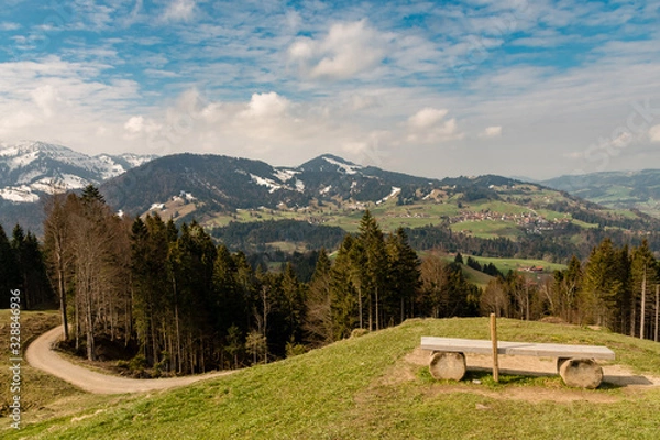 Fototapeta A bench on the Hündle, a peak in the Allgäu, with a magnificent view over snow-covered mountains and green valleys.