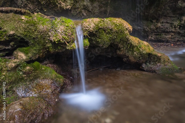 Fototapeta Small waterfall in the forest with a water jet and mossy tree roots. 