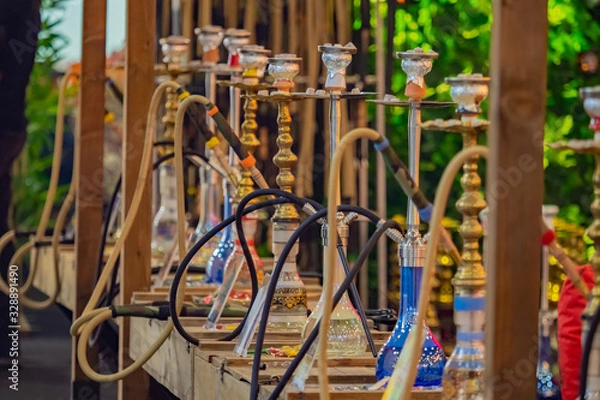 Fototapeta Several hookahs are standing on the street. Multi-colored hookahs on a wooden rack. Concept - hookah shop. Hookah party takes place on the street. Hookah of different types exhibited on the street