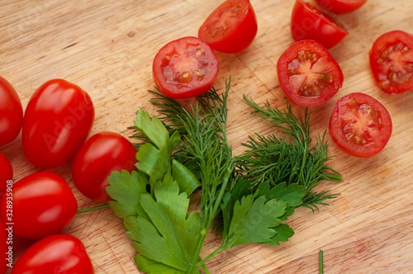 Fototapeta Ripe cherry tomatoes with parsley and dill in a wooden cutting board, top view