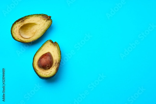 Fototapeta A rotten avocado cut in half on blue background.