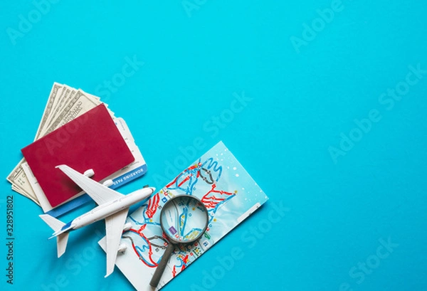 Fototapeta Travel accessories and objects on a blue background with a top view and copy space.Airplane and passport, money, map, ticket, sunglasses. Travel background for travel agency banner advertisement. 