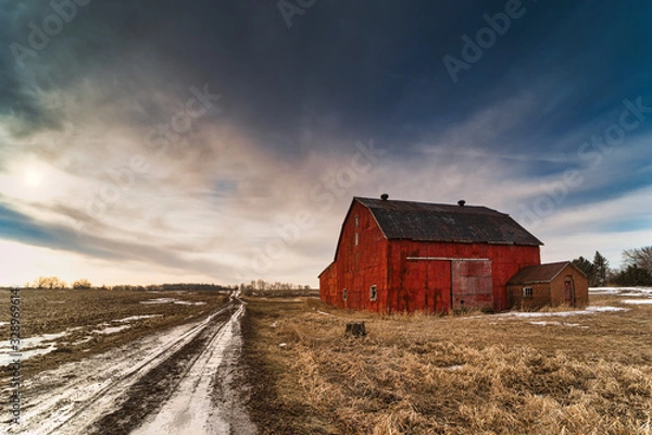 Fototapeta Stunning dramatic sunsets in rural farm country with barns and cold fields with rainbow.