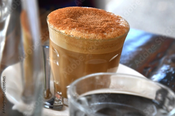Obraz Frothy top coffee in glass at cafe table.