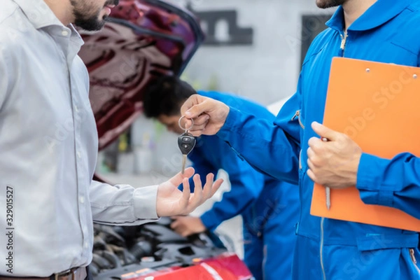 Obraz Close up of young smiling men mechanic Hand over keys to customers businessman of a car. Concept for key car rental