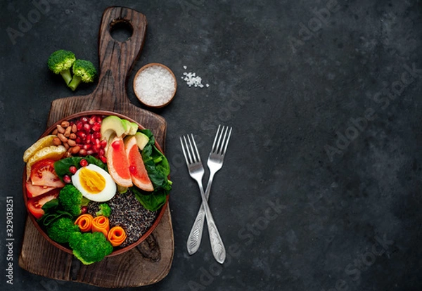 Fototapeta Bowl of Buddha,quinoa, orange, avocado, grapefruit, tomato, pomegranate, spinach, carrots, broccoli, egg in a bowl on a stone background, with copy space for your text