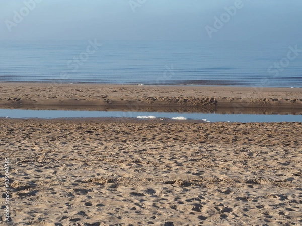 Fototapeta Footprints in the sand of the seashore. Light fog. Blue sky.