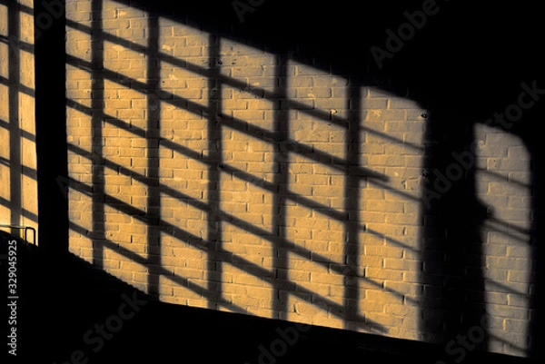 Fototapeta Dark shadow on a stonework wall illuminated by golden sunlight - concept dramatic contrast film noir mystic interior texture background surface structure window close up detail evening sunset sunrise