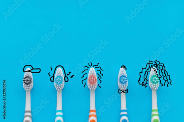 Obraz Colorful toothbrushes on a blue background in the form of cartoon characters. The view from the top. Close up. Concept of family hygiene.