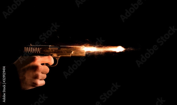 Obraz The hand presses the trigger of the gun and the flame from the shot escapes from its muzzle