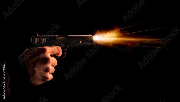 Fototapeta The hand presses the trigger of the gun and the flame from the shot escapes from its muzzle