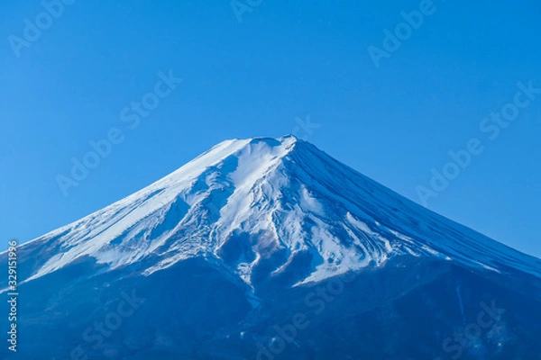 Fototapeta A distant, close up view on Mt Fuji in Japan on a clear, wintery day. Inaccessible slopes of the mountains are covered with a thick layer of snow. Holly mountain of Japan.