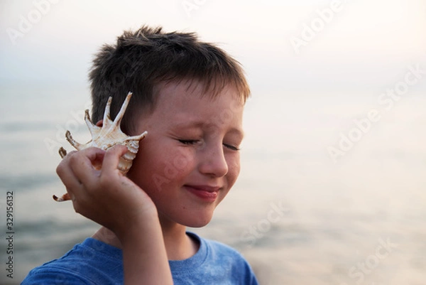Obraz A blind boy listens to the sound of the sea, leaning a seashell against his ear.