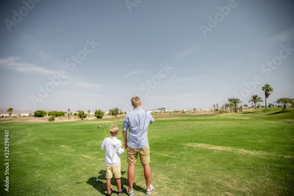 Obraz Father has fun and teaches his son to play golf on the green grass.