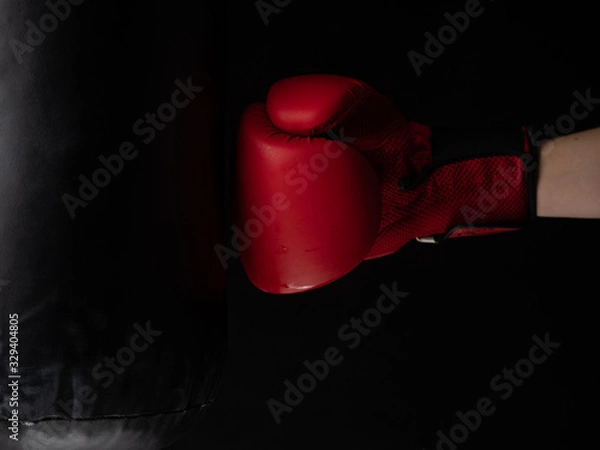 Obraz red boxing glove hitting the punching bag on black background