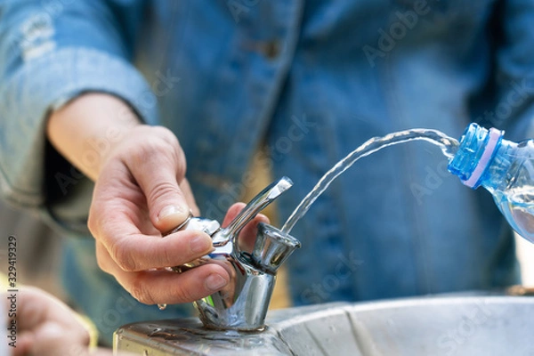 Fototapeta Filling a bottle with drinking water in a public drinking fountain.