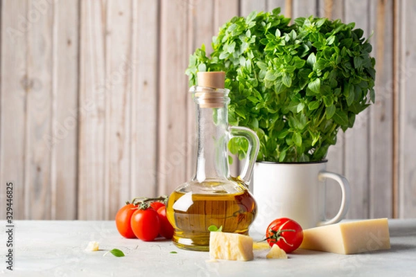 Fototapeta Olive oil in a jug, tomatoes, Parmesan cheese and Green Greek mini Basil in a pot on a table. Space for the test.
