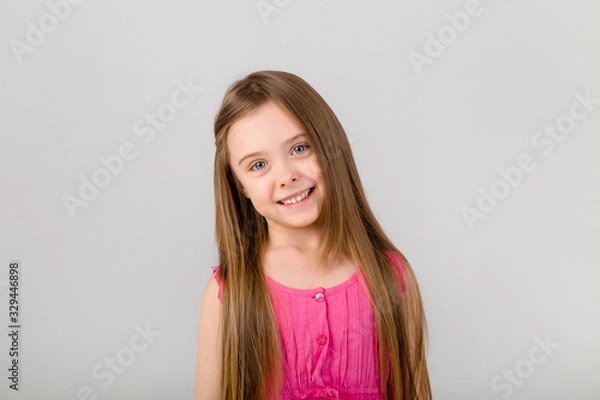 Fototapeta portrait of a little girl with long hair in pink clothes on a white background. happy baby girl smiling on white background isolate