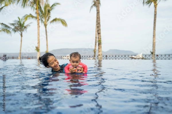 Fototapeta asian mother holds her little baby while swimming and playing in the pool