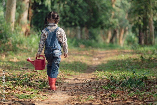 Fototapeta Asian little girl holding red watering tree walking in nature. First learning of little children. Happy family concept. Rear view shot