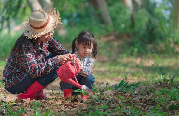 Obraz Asian little girl with mom planting and watering tree in nature. First learning of little children.
