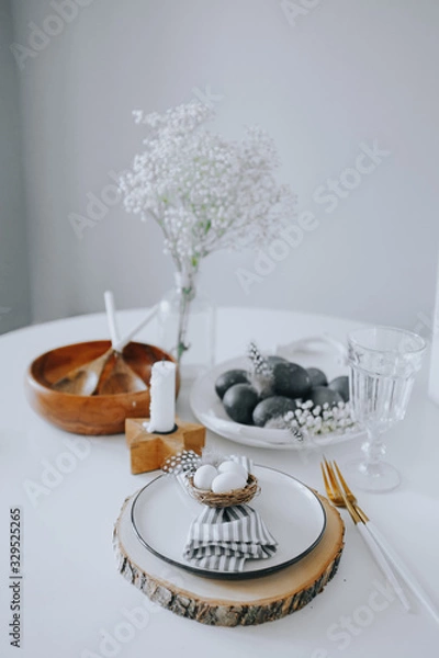 Fototapeta Easter table setting with white plate, gray textile napkin, candles, quail and chicken eggs and blossom branch.Mock up easter card