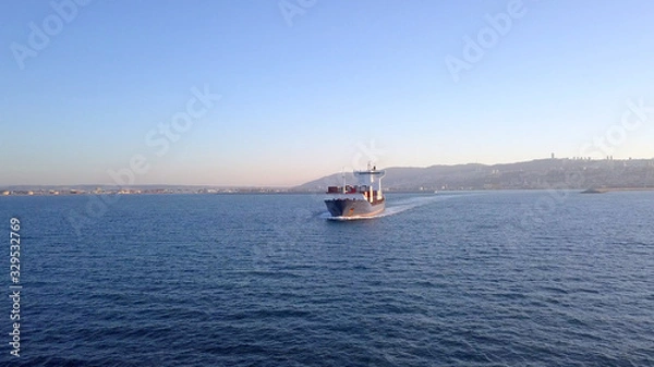 Fototapeta Aerial shot of container ship in ocean. Loaded vessel moves at calm water.
