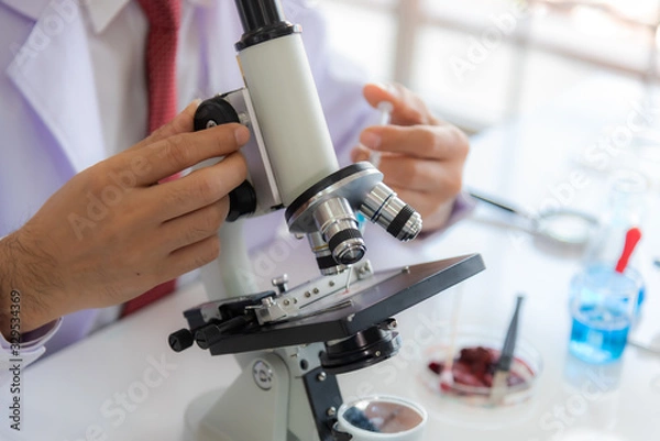 Fototapeta Close up: scientist woman analyzing covid 19 sample with microscope and holding coronavirus covid 19 blood sample tube on hand in laboratory, coronavirus covid 19 vaccine research