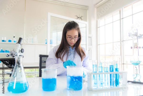 Obraz In a modern laboratory, a female chemist conducts experiments on the synthesis of compounds using a dropper and a solution in a test tube. COVID-19