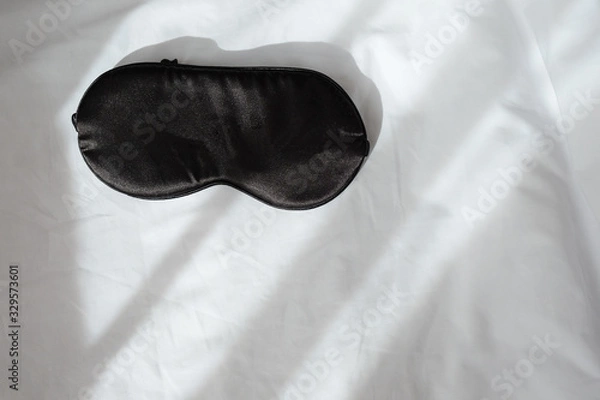 Fototapeta Silk black sleep mask without inscription on white rumpled sheets. Top view, flat lay. Horizontal. Copy spase. Concept of rest, awakening, sleep. For social media, blog. Minimal style