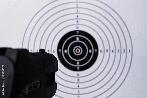 Fototapeta Background with a pistol aimed at a round target with a red dot from a laser sight in the center. Business Goal Achievement Concept