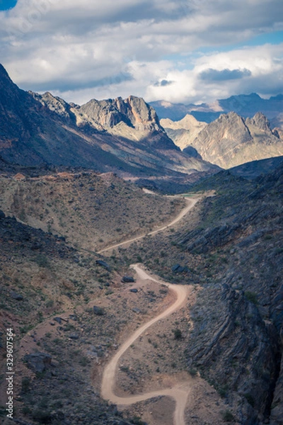 Fototapeta View of the dirt road between mountains on a cloudy day in Jebel Shams, Oman