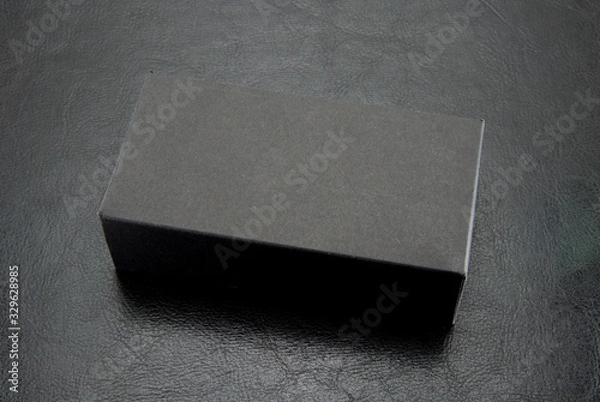 Fototapeta Black, rectangular, paper box matte color on a black leather background. Cardboard package.