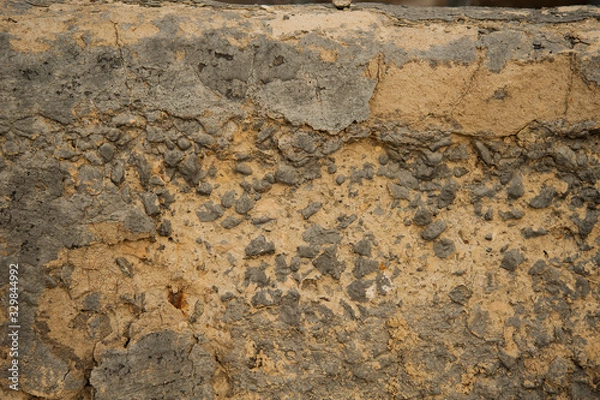 Fototapeta texture of a sand wall with grey stones,the yellow-grey background is cracked and destroyed,the background of yellow sand color with gray details