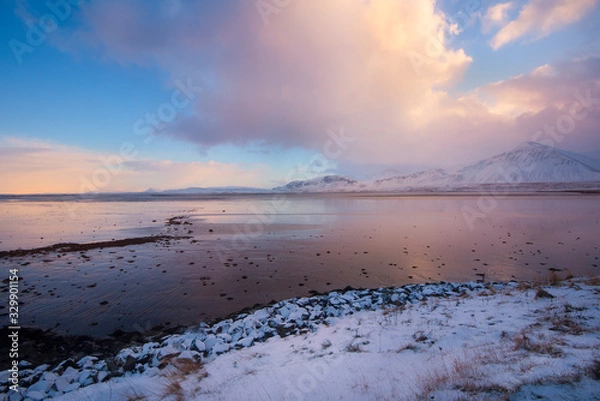 Fototapeta Dark clouds developing in a blue sky with a pink horizon over the coast of Iceland at sunset, with a rocky shoreline in the foreground  