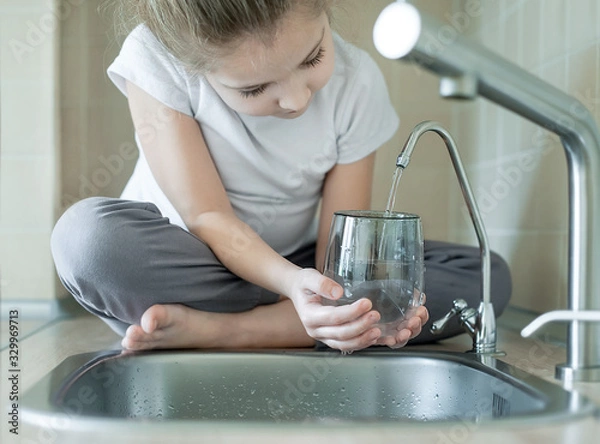 Obraz Child holding a glass under stream of clear transparent cold water from a tap. Close up shot of a young girl pouring a glass of fresh water from a kitchen faucet. Healthy Nutrition. World Water Day